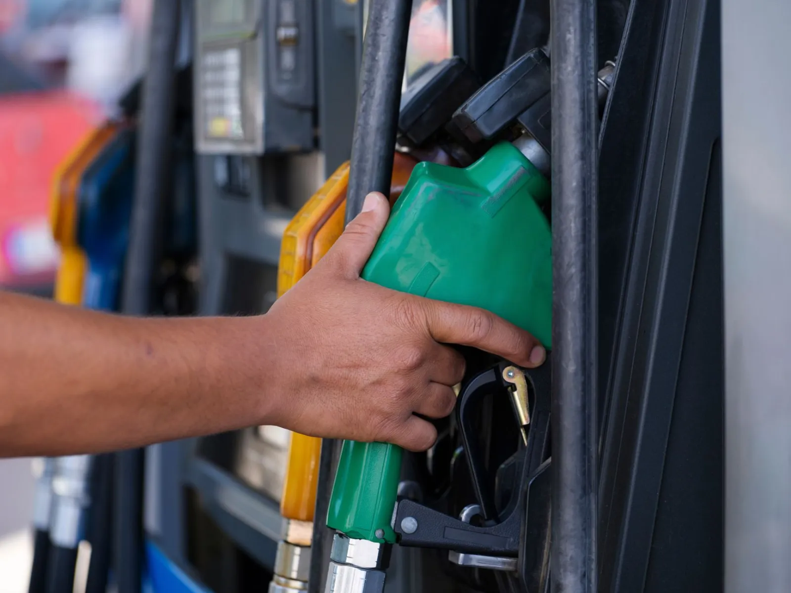 Close-up of a hand holding a green fuel nozzle at a gas pump station outdoors.