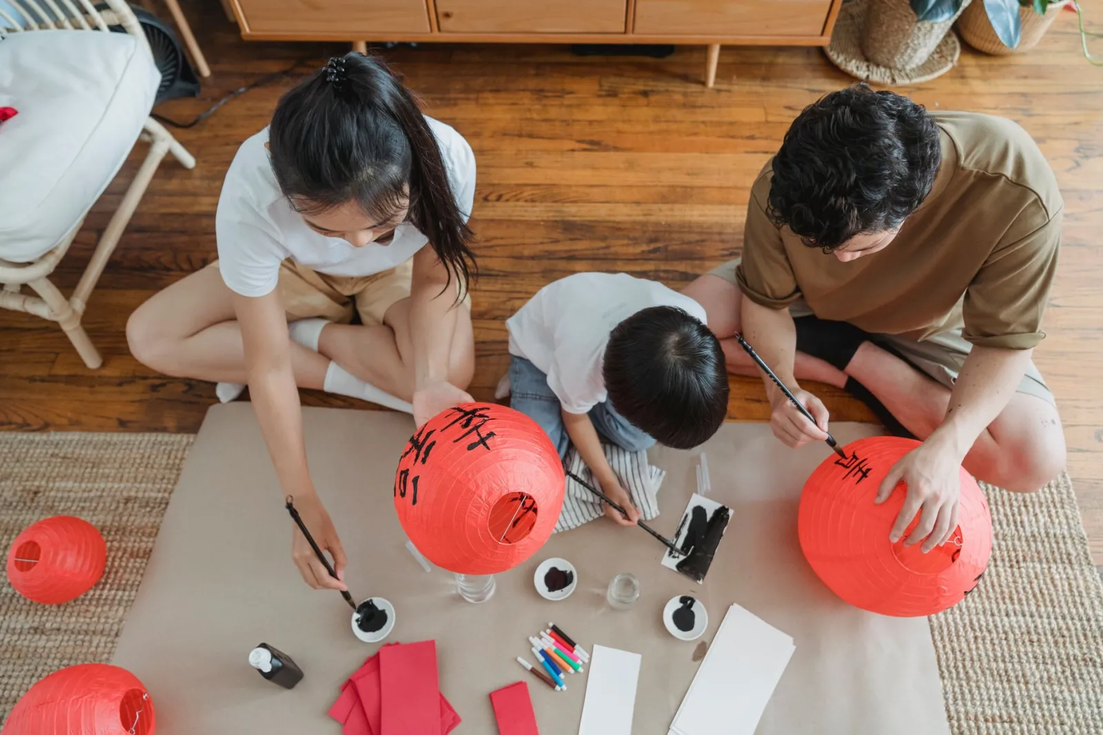 Family enjoying a creative bonding session while painting red lanterns during the day.