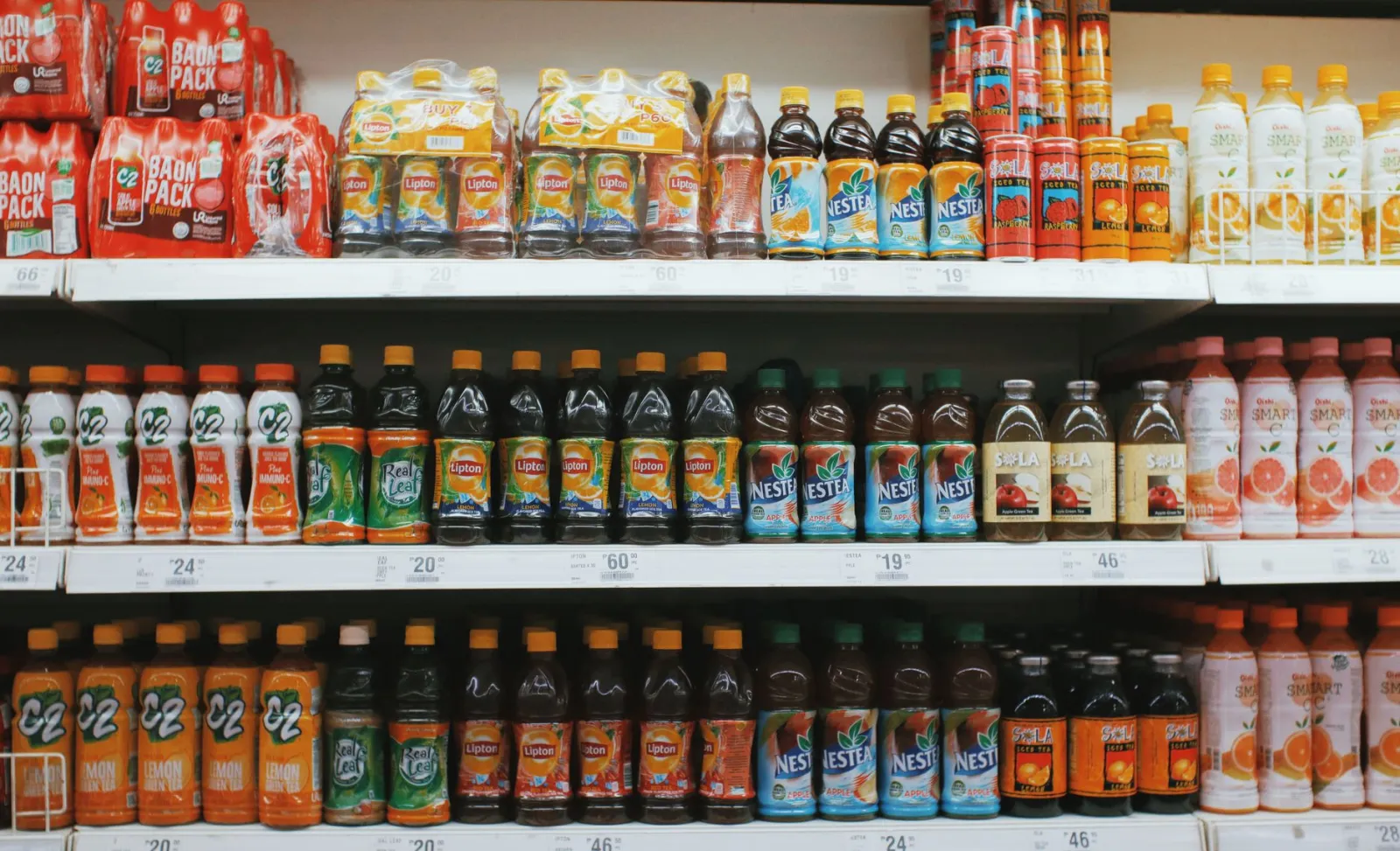 Rows of colorful plastic bottles with lemonades placed on light shelves in supermarket